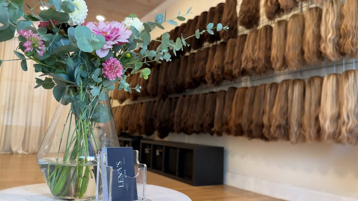 The Lena's Wigs studio: a vase of flowers and a Lena's Wigs card in front of a wall of wigs